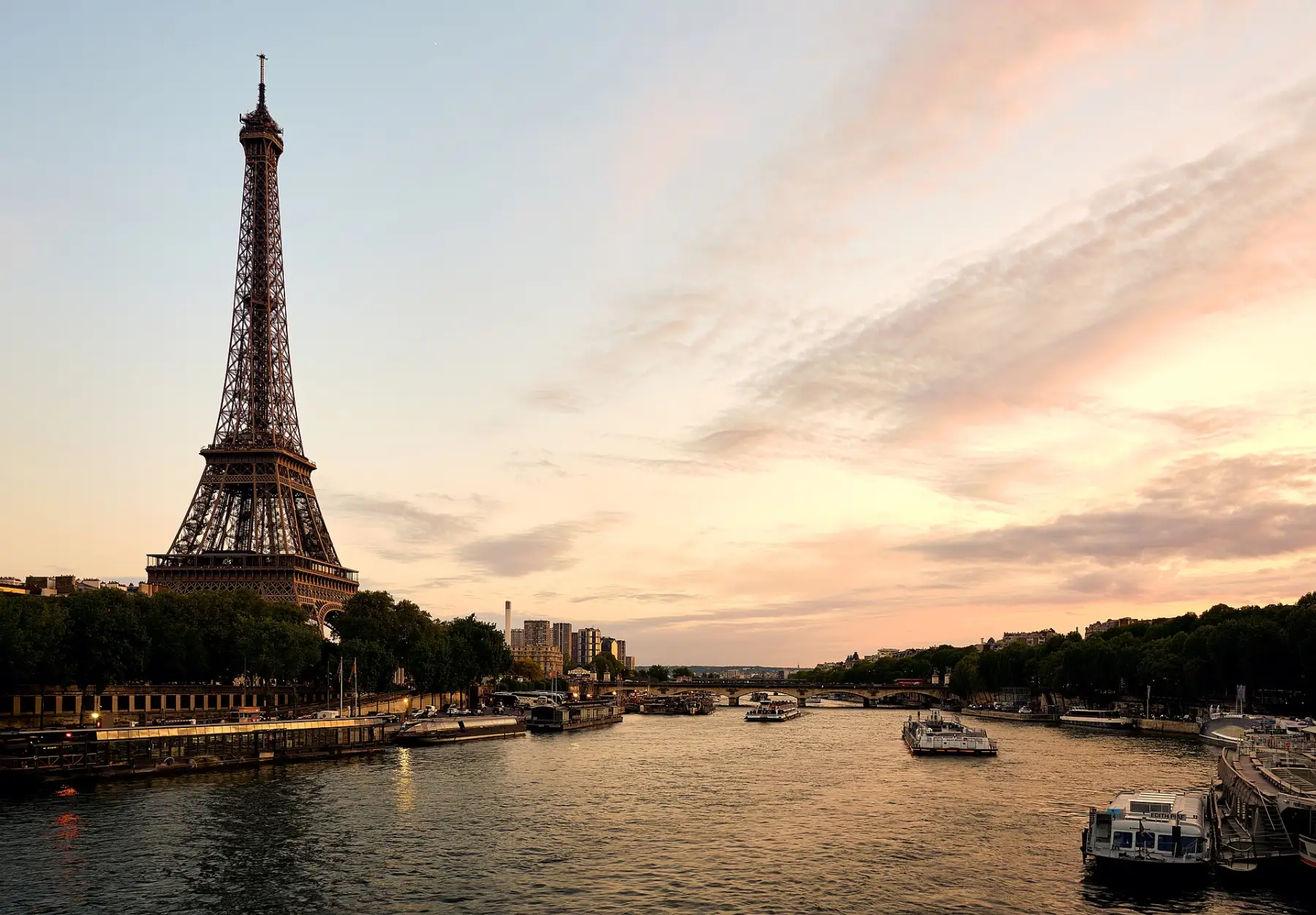 The Eiffel Tower above the Seine at dusk, boats moored along the quay.